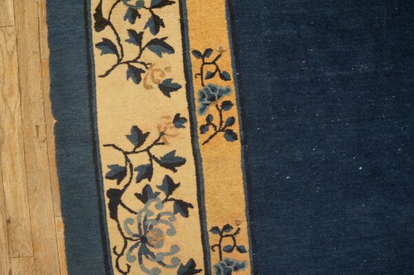 Navy blue rug field bordered by a wide beige panel with blue flowers on light wood flooring.