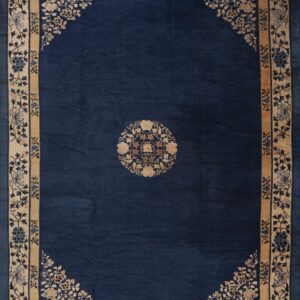 Navy blue rug with a small central medallion and wide beige border detailed with floral motifs.