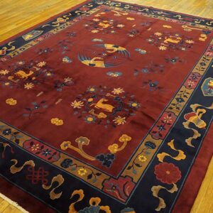 Deep red rug with a complex navy border and gold crane and deer motifs on a wood floor.