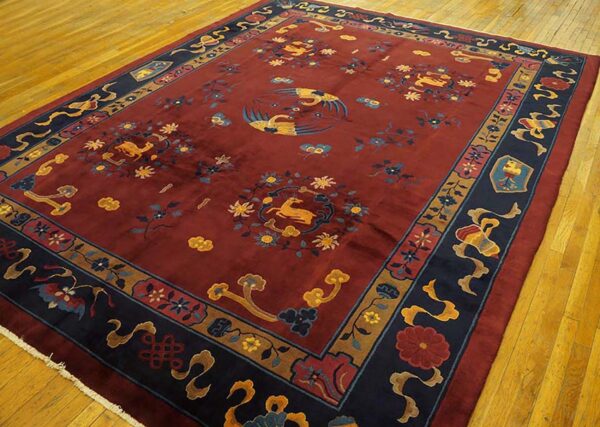 Deep red rug with a complex navy border and gold crane and deer motifs on a wood floor.