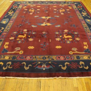 Low-pile burgundy rug with blue and gold Asian motifs and a navy border rests on glossy hardwood.