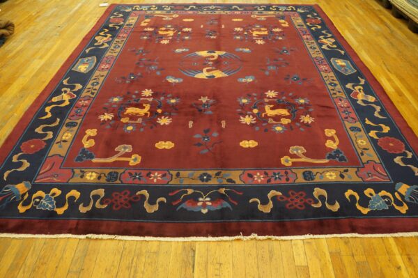 Low-pile burgundy rug with blue and gold asian motifs and a navy border rests on glossy hardwood.