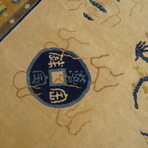Pale yellow rug detail showing a navy blue coin and dragon pattern with orange line accents.