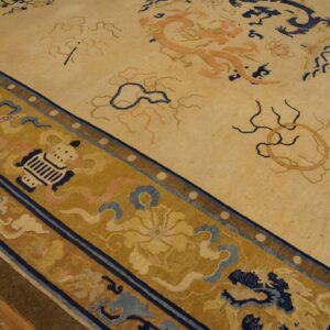 Pale yellow rug with peach and navy dragon patterns features a wide golden border on wood flooring.