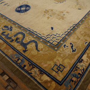 Low-pile rug corner showing cream field and gold border with blue dragons on worn wood flooring.