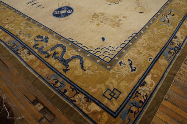 Low-pile rug corner showing cream field and gold border with blue dragons on worn wood flooring.