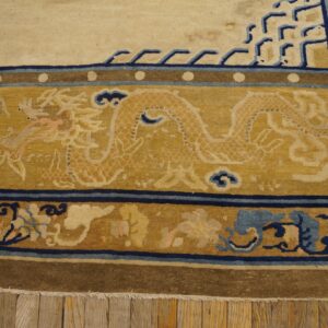 Detail shot of a cream and gold rug border with dragon and blue fretwork patterns on wood plank flooring.