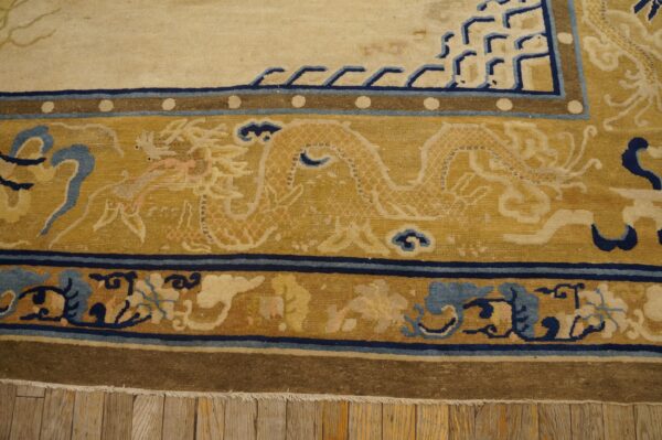 Detail shot of a cream and gold rug border with dragon and blue fretwork patterns on wood plank flooring.