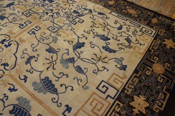 Cream and indigo floral rug with a complex dark border rests on rustic wooden flooring.
