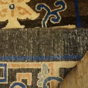Dark brown, tan, and blue patterned rug corner folded to display the low pile backing on wood flooring.