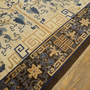 Cream rug with swirling blue vines and Greek key borders rests on distressed yellow hardwood flooring.