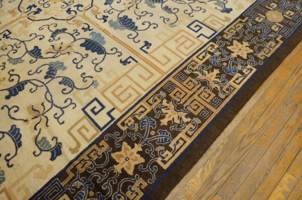 Cream rug with swirling blue vines and greek key borders rests on distressed yellow hardwood flooring.