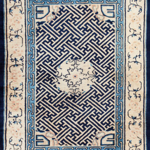 A high-contrast rug with a navy geometric key pattern field bordered by light blue and cream floral motifs.
