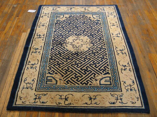 Cream and blue rug featuring a dense central geometric pattern is displayed on a wide plank wood floor.