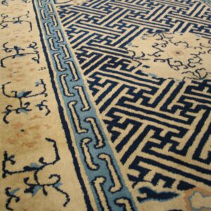 Beige and blue high-pile rug with geometric field pattern and scrolling borders rests on hardwood floor.