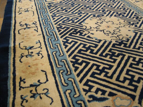 Beige and blue high-pile rug with geometric field pattern and scrolling borders rests on hardwood floor.