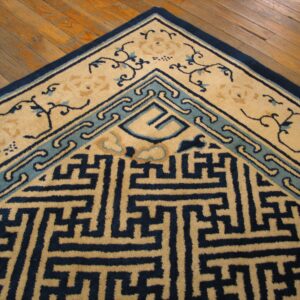 Corner of a navy, teal, and beige rug featuring geometric and scrolling motifs on a wood floor.