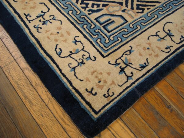 Tan and navy patterned rug corner with blue scroll motifs rests on rustic wooden floorboards.