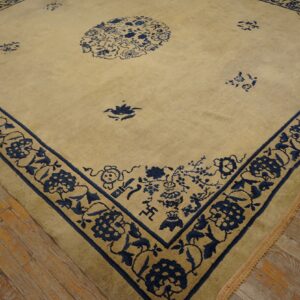 A beige rug with a wide indigo blue floral border and central medallion rests on worn wood flooring.