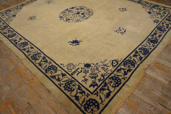 A beige rug with a wide indigo blue floral border and central medallion rests on worn wood flooring.