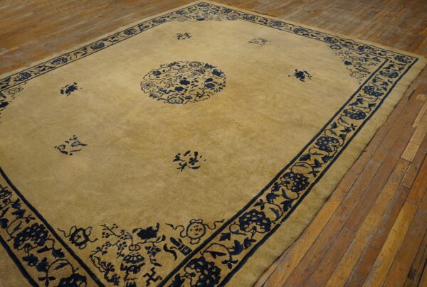 Golden beige rug with a dark blue floral medallion and ornate border on distressed wood floors.