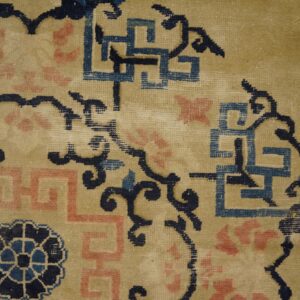 Low pile rug texture showing navy, pink, and blue fretwork motifs on a tan background.