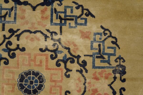 Low pile rug texture showing navy, pink, and blue fretwork motifs on a tan background.