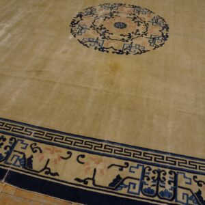 Large tan rug with a central blue and pink medallion and a detailed navy and Greek key border on wood floor.