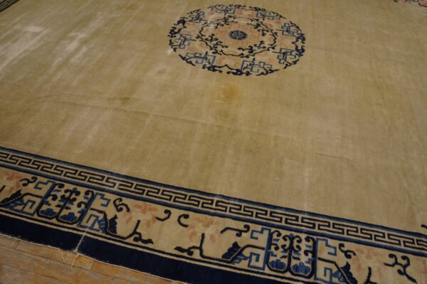 Large tan rug with a central blue and pink medallion and a detailed navy and greek key border on wood floor.
