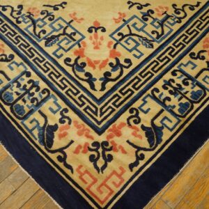 Beige rug with a navy border, blue key pattern, and coral flowers visible on wood flooring.