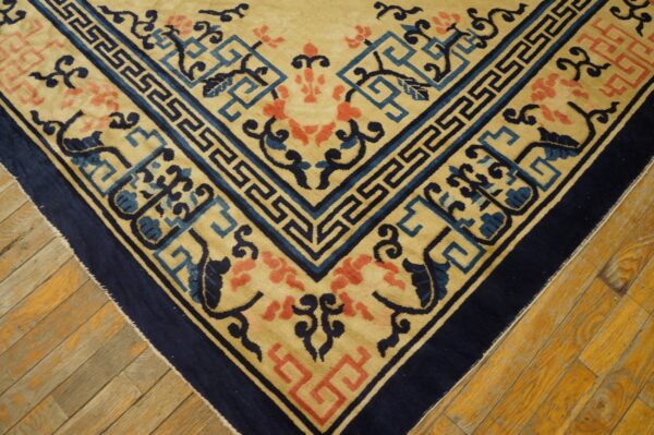 Beige rug with a navy border, blue key pattern, and coral flowers visible on wood flooring.