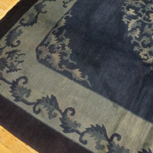 Close-up of a high-pile rug with a navy, sage, and dark blue floral border on light wood flooring.