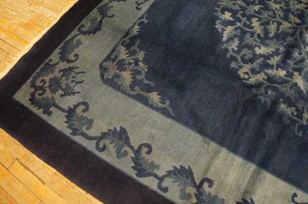 Close-up of a high-pile rug with a navy, sage, and dark blue floral border on light wood flooring.