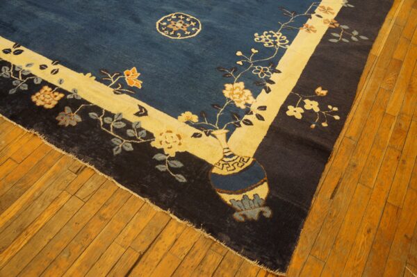 Navy and cream floral rug featuring a vase pattern borders old amber-toned wooden flooring.