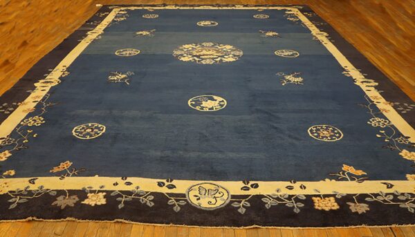Deep blue rug with contrasting beige medallion and wide floral borders on light wood floor.