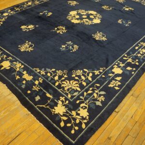 Low-pile navy rug with yellow and teal floral patterns displayed on distressed hardwood flooring.