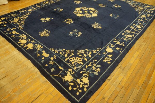 Low-pile navy rug with yellow and teal floral patterns displayed on distressed hardwood flooring.