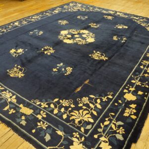 Navy blue rug featuring yellow and teal floral designs rests on golden-toned wooden planks.