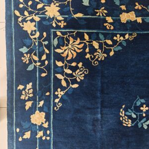 Close-up of a navy blue rug corner with gold and pale blue floral vines and a thin striped border.