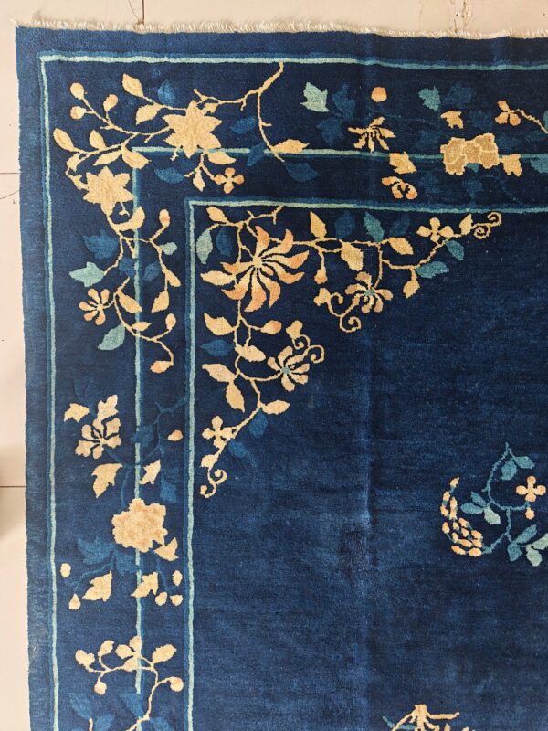 Close-up of a navy blue rug corner with gold and pale blue floral vines and a thin striped border.