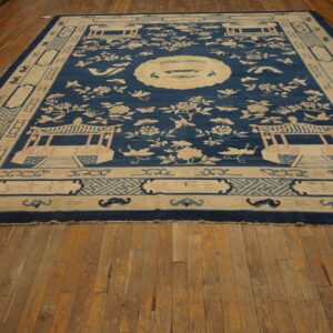 Navy and cream rug featuring pavilions and floral sprays bordered by geometric patterns rests on distressed wood flooring.