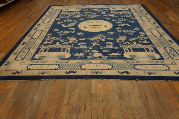 Navy and cream rug featuring pavilions and floral sprays bordered by geometric patterns rests on distressed wood flooring.