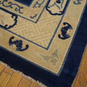Navy blue, light blue, and tan rug with scrollwork borders rests on distressed wood planks.