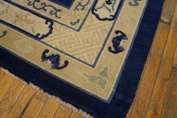 Navy blue, light blue, and tan rug with scrollwork borders rests on distressed wood planks.