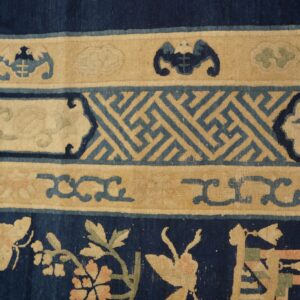 Close view of a navy, beige, and blue rug featuring floral and geometric borders on wooden flooring.