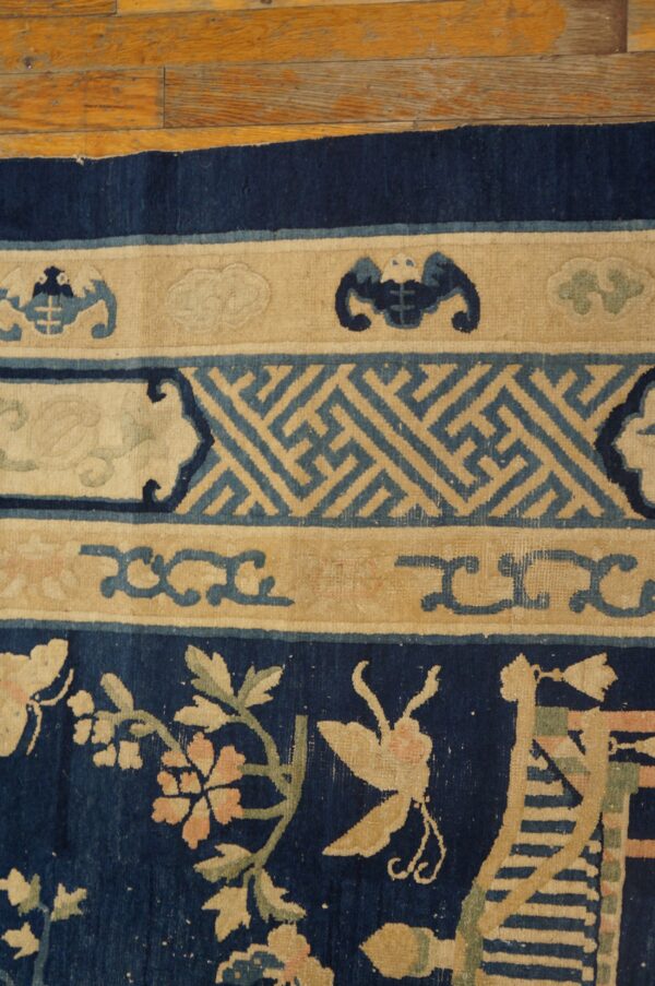 Close view of a navy, beige, and blue rug featuring floral and geometric borders on wooden flooring.