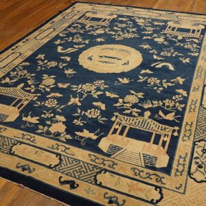 A large navy blue rug with a light beige scenic pattern featuring pavilions, flowers, and a medallion, lying on a wooden floor.