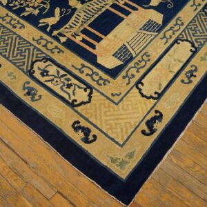 Intricate yellow and navy border of a patterned rug, including geometric and floral designs, rests on wood floors.