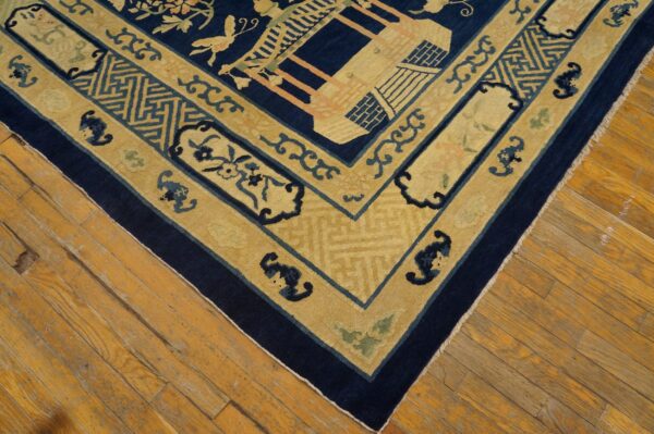 Intricate yellow and navy border of a patterned rug, including geometric and floral designs, rests on wood floors.
