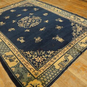 Navy blue rug with a pale yellow medallion and complex light blue borders lies on distressed wood planks.